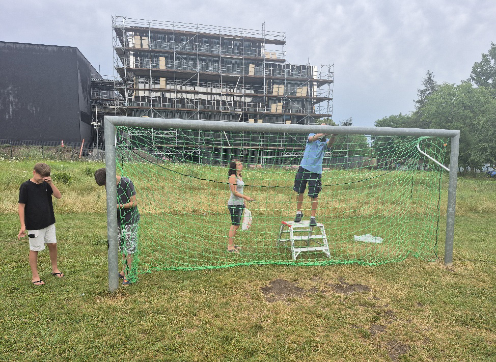 Foto: O. Merzenich Zwei Erwachsende und zwei Jugendliche befestigen ein Netz an einem Fußballtor.